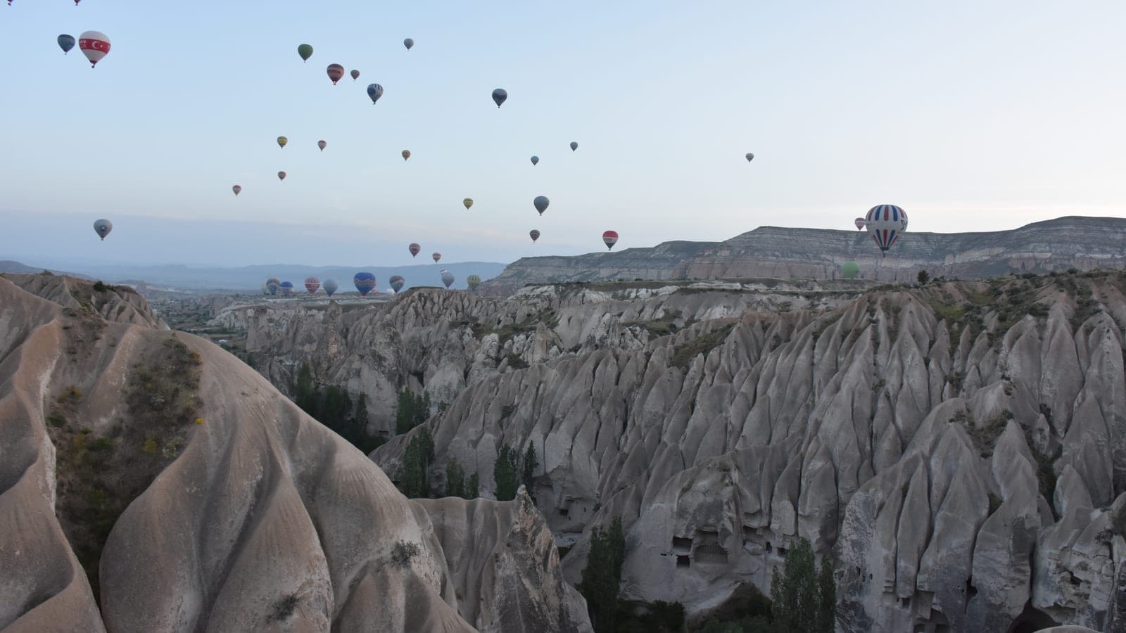 Ballons treiben kurz nach Sonnenaufgang tief über den Tälern