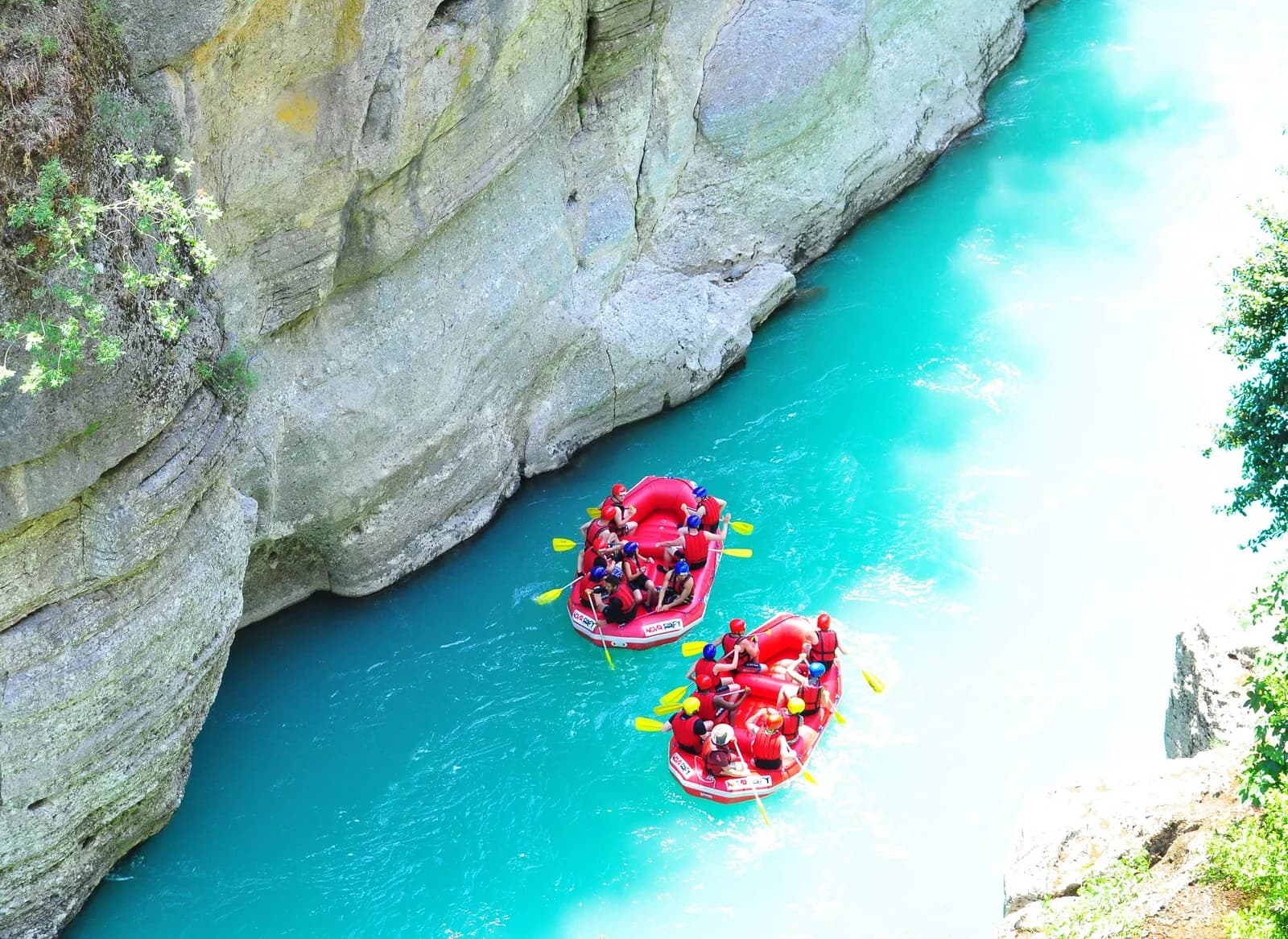 Köprülü Kanyon nehrinde can yelekleri ve kasklarıyla rafting botunda kürek çeken mutlu insanlar